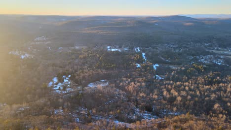 Flying-over-a-golden,-sun-covered-valley-at-sunset-during-winter-with-light-snow-on-the-ground