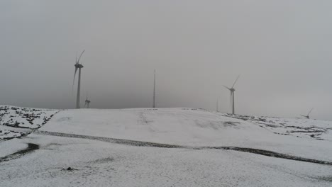 Winter-mountain-countryside-wind-turbines-on-rural-highlands-aerial-view-cold-snowdrift-valley-hillside-push-in