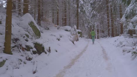 Adult-man-in-green-neon-outfit-running-in-frosty-pine-forest-on-snowy-trail-during-cold-winter-day---forward,-slow-motion