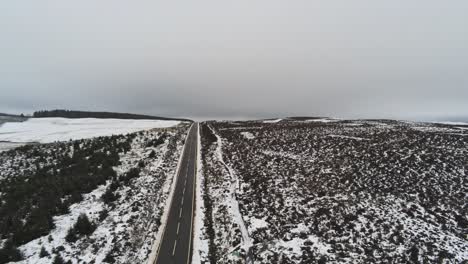 Long-road-aerial-into-distance-across-highland-snowy-countryside-moors-descending-shot