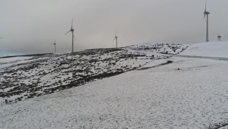 Winter-mountain-countryside-wind-turbines-on-rural-highlands-aerial-view-cold-snowy-hillside-rising-pan-right