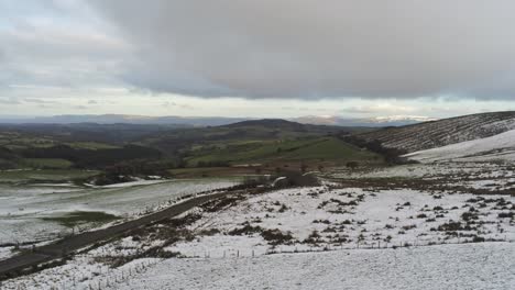 Snowy-rural-seasonal-winter-valley-countryside-aerial-agricultural-farmland-landscape-pan-right