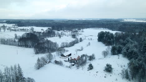 Ascend-aerial-top-down-of-snow-covered-holiday-cottage-surrounded-by-rural-white-winter-landscape-during-christmas-time