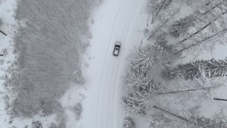 Aerial-tracking-shot-of-a-suv-car-on-snowy-road-turning-right-in-middle-of-snow-covered-trees-in-frozen-forest,-on-a-winter-day---drone-shot,-tracking,-top-down