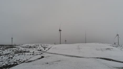 Winter-mountain-countryside-wind-turbines-on-rural-highlands-aerial-view-cold-snowy-valley-hillside-lowering-left