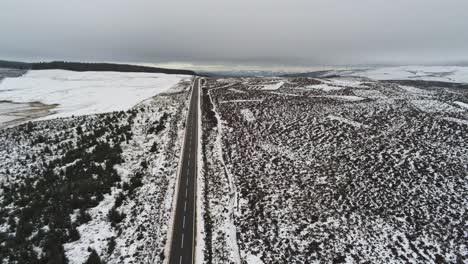 Lowering-to-long-road-aerial-into-distance-across-highland-snowy-countryside-moors