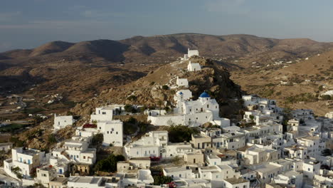 Drone-aerial-footage-of-Chora-town-with-churches-on-the-hill-at-sunset,-white-building-in-Ios-Greece