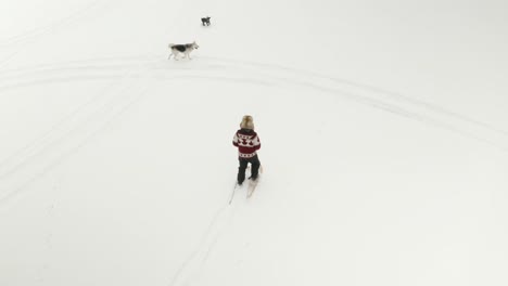 Adult-man-in-large-fur-hat,-walks-and-plays-in-traditional-snowshoes-on-frozen-lake-with-his-pet-dogs-in-northern-Canada