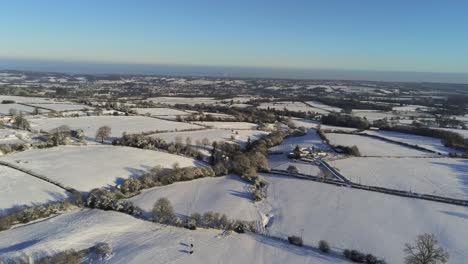 Cold-snowy-winter-British-patchwork-farmland-countryside-rural-scene-aerial-pan-left-forward-at-sunrise