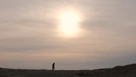 Extreme-wide-shot-of-a-man-running-across-the-desert-at-sunset