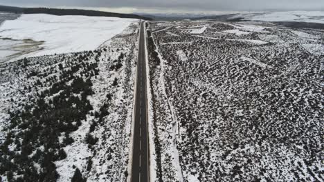 Long-road-aerial-birdseye-tilt-up-across-highland-snowy-countryside-moors