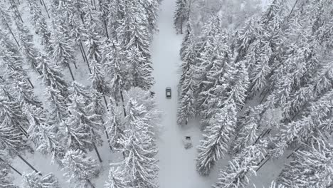 Aerial-epic-view-overlooking-a-car-on-snowy-road-in-snow-covered-forest,-on-a-winter-overcast-day---drone-shot,-tracking-shot,-overhead