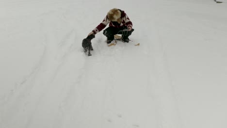 Erwachsener-Mann-Mit-Großer-Pelzmütze-Winkt-In-Traditionellen-Schneeschuhen-Auf-Einem-Zugefrorenen-See-Mit-Seinen-Hunden-Im-Norden-Kanadas-In-Die-Kamera