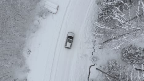 Aerial-view-shot-of-a-car-on-the-snowy-road-turning-right-in-middle-of-snow-covered-trees-in-frozen-forest,-on-a-winter-day---drone-shot,-tracking-shot,-top-down