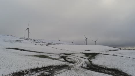 Winter-mountain-countryside-wind-turbines-on-rural-highlands-aerial-view-cold-snowy-valley-hillside-pull-back-rising-shot