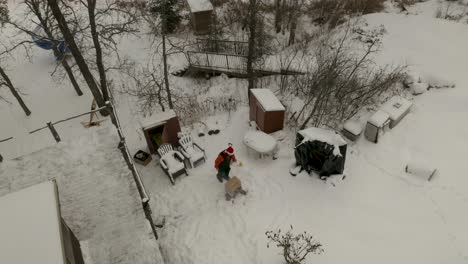 Aerial-shot-of-a-Canadian-male-in-Santa-hat-building-a-fire-outside-of-his-snow-covered-winter-cabin