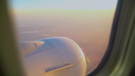 Scenic-view-out-the-window-of-an-airplane-with-a-pink-sunset-sky-and-view-of-the-turbine-engine