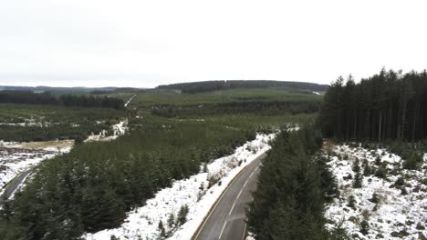 Snowy-curved-winter-woodland-road-aerial-reversing-view-following-forest-tree-landscape