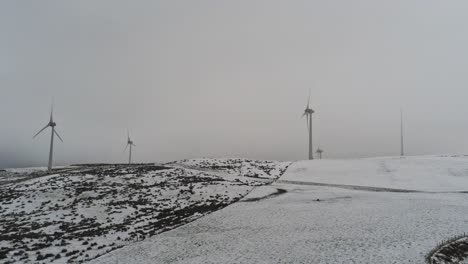 Winter-mountain-countryside-wind-turbines-on-rural-highlands-aerial-view-cold-blizzard-valley-hillside-pan-left