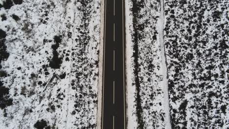 Long-empty-road-aerial-birdseye-reversing-along-highland-snowy-countryside-moors