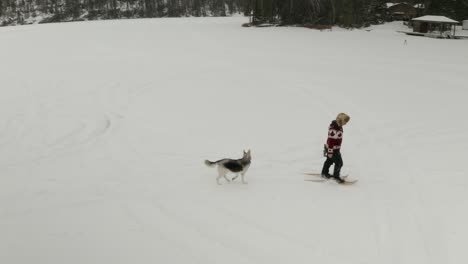 Erwachsener-Mann-Mit-Großer-Pelzmütze,-Geht-Und-Spielt-In-Traditionellen-Schneeschuhen-Auf-Einem-Zugefrorenen-See-Mit-Seinen-Hunden-Im-Norden-Kanadas