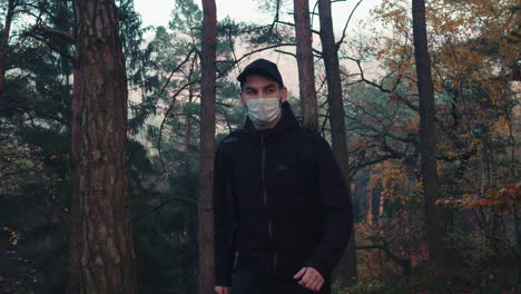 Caucasian-man-walking-in-forest-with-medical-face-mask,-life-after-covid-pandemic,-middle-shot-side-view