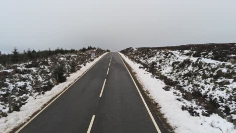 Long-road-aerial-into-distance-across-highland-snowy-countryside-moors-low-forward-push-in