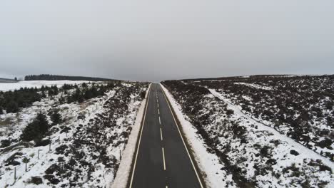 Long-road-aerial-reversing-revealing-distance-across-highland-snowy-countryside-moors