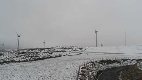 Winter-mountain-countryside-wind-turbines-on-rural-highlands-aerial-rising-left-view-cold-snowy-valley-hillside