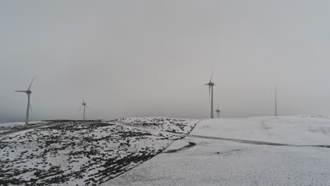 Winter-mountain-countryside-wind-turbines-on-rural-highlands-aerial-rising-pan-right-view-cold-snowy-valley-weather