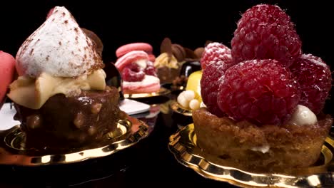 macro-view-moving-past-patisserie-on-black-reflective-background,-probe-lens-view-of-sweet-pastry-and-small-cakes