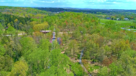 Aerial-View-of-Spring-Time-Colors-of-a-Forest-with-a-Covered-Bridge-and-Rail-Road-Track-on-a-Sunny-Day