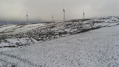 Winter-mountain-countryside-wind-turbines-on-rural-highlands-aerial-right-pan-shot-across-cold-snowy-valley-hillside