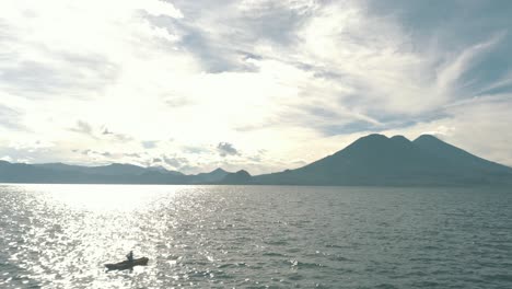 Drone-aerial-flying-over-lake-Atitlan,-Guatemala-surrounded-by-beautiful-volcanoes-and-rotating-around-a-man-kayaking