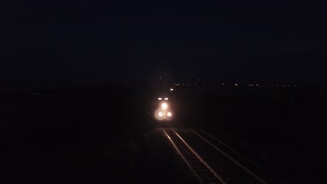 Freight-train-lights-prairie-railroad-tracks-on-dark-purple-night