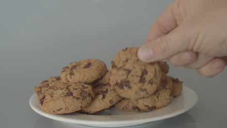 Hand-placing-chocolate-chip-cookies-on-pile-of-cookies---wide