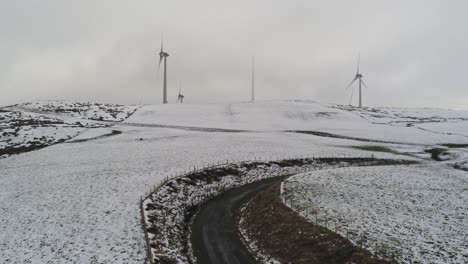 Winter-mountain-countryside-wind-turbines-on-rural-highlands-aerial-view-cold-snowy-valley-hillside-rising-tilt-up