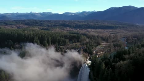 Aerial-flyover-Snoqualmie-Falls-Waterfall-with-mist-in-the-valley-and-beautiful-nature-landscape-with-pine-trees-and-mountains-in-background