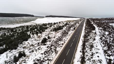 Long-road-aerial-into-distance-across-highland-snowy-countryside-pull-back-rising