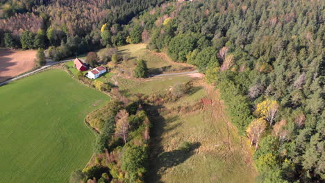 Rural-house-facing-vast-empty-field-in-middle-of-woods,-aerial-drone-rising