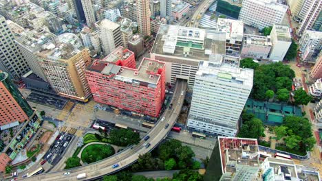 Traffic-passing-through-a-Car-park-building-in-downtown-Hong-Kong,-with-city-mega-buildings,-Aerial-view