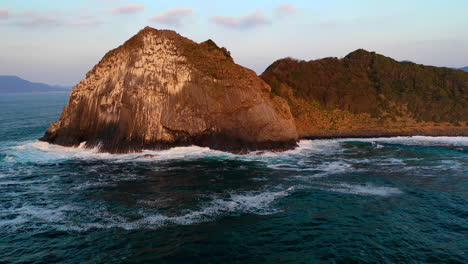 Rotating-drone-shot-of-sun-setting-on-large-rock-in-ocean-at-Kyushu-Japan