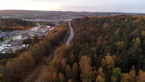 Aerial-drone-flying-above-road-to-Gothenburg-in-suburbs-area,-autumn-forest,-day