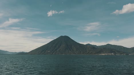 Drone-aerial-view-flying-close-by-the-blue-water-of-lake-Atitlan,-Guatemala-and-a-big-volcano-in-the-background
