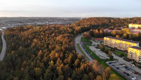 Drone-pull-back-shot-over-forest-revealing-high-rise-apartment-blocks-during-sunrise