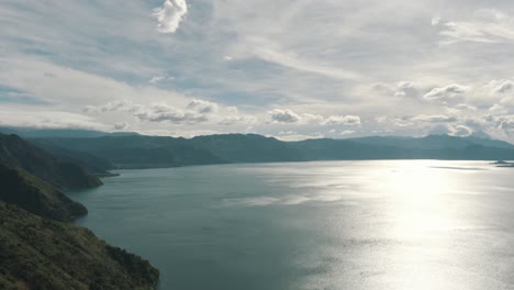 Drone-aerial-overview-of-lake-Atitlan,-Guatemala-surrounded-by-volcanoes-and-mountains-during-a-beautiful-day