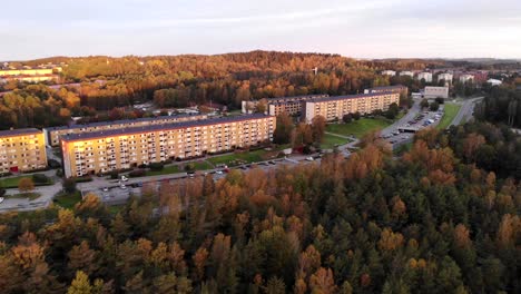 Suburb-area-outside-Gothenburg,-Sweden,-aerial-view-drone-flying-backwards-at-sunset-above-roadside-forest