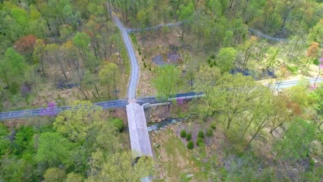 Aerial-View-of-Spring-Time-Colors-of-a-Forest-with-a-Covered-Bridge-and-Rail-Road-Track-on-a-Sunny-Day