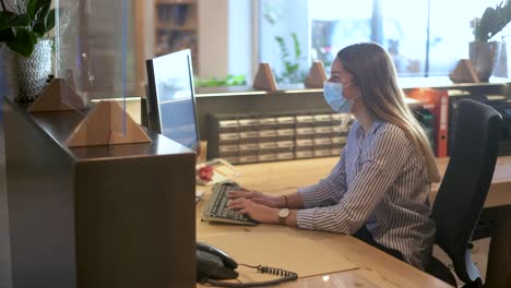 Receptionist---office-employee-works-with-face-mask-on-a-computer-in-the-reception-area---Coronavirus-tourism-footage