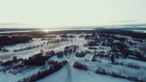 Aerial-view-of-snowy-winter-Christmas-landscape-far-north-nordic-Scandinavia-Swedish-Norwegian-hills-forest-mountain-top-as-sun-sets-late-afternoon-cold-road-empty-wasteland-lonely-houses-and-homes